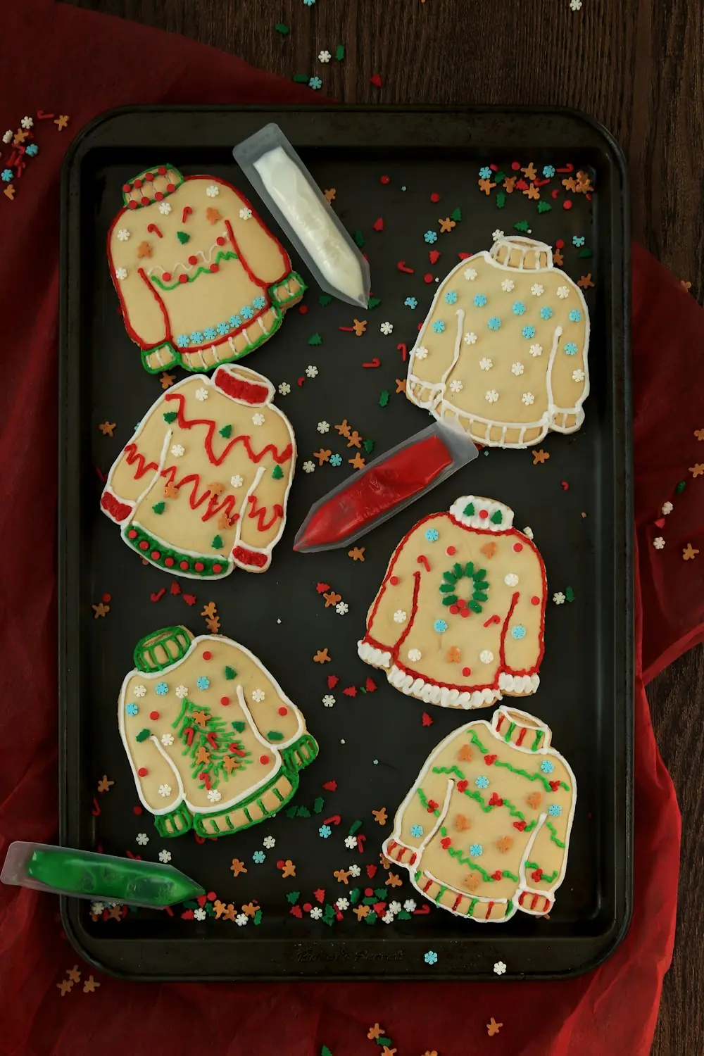 A baking tray of sweater-shaped Christmas cookies decorated with icing and sprinkles